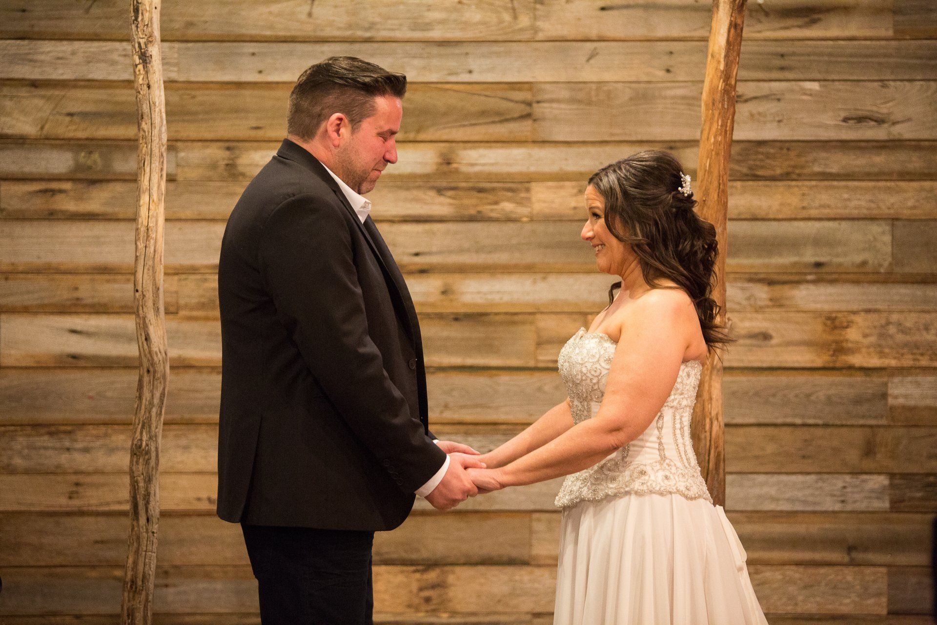 A bride and groom are holding hands in front of a wooden wall.