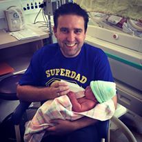 A man in a blue shirt is holding a newborn baby in his arms.