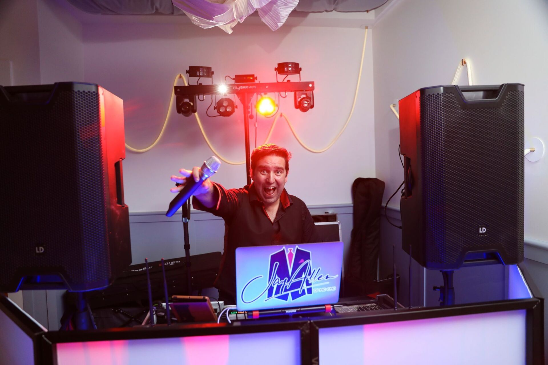 A man is standing in front of a dj booth holding a microphone.