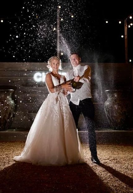 A bride and groom are standing next to each other holding a bottle of champagne.