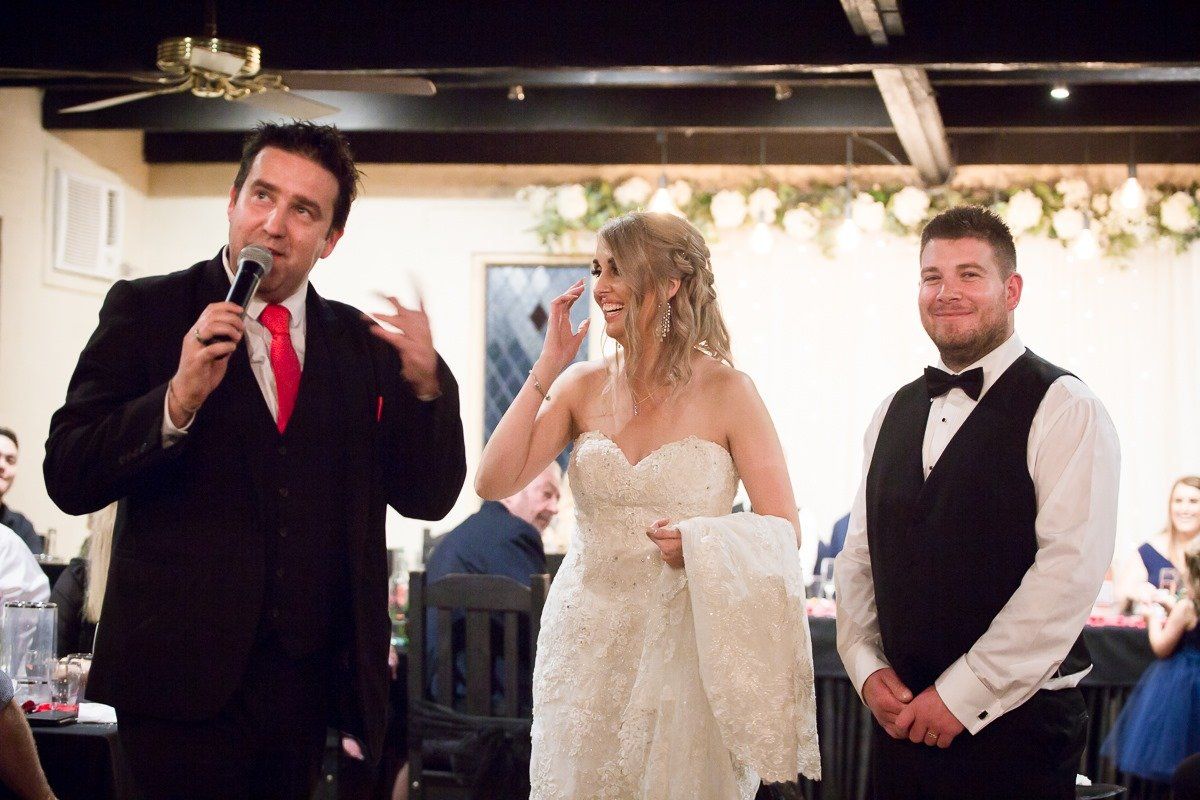 A man is giving a speech to a bride and groom at a wedding reception.