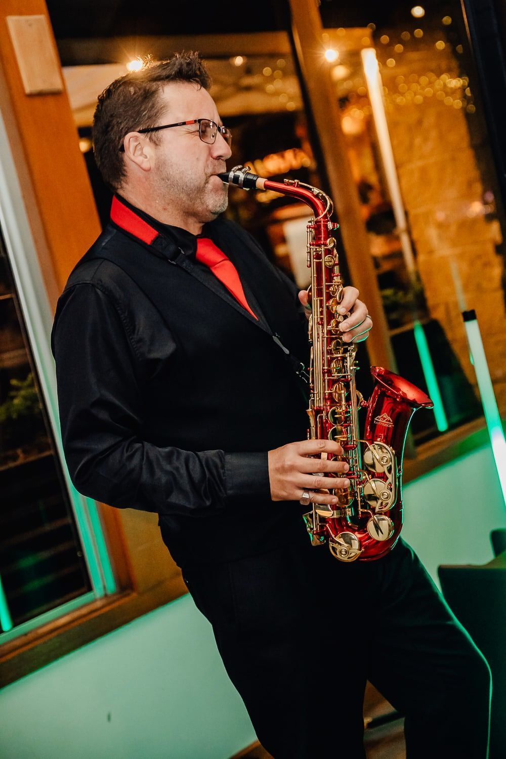 A man in a black shirt and red tie is playing a saxophone.