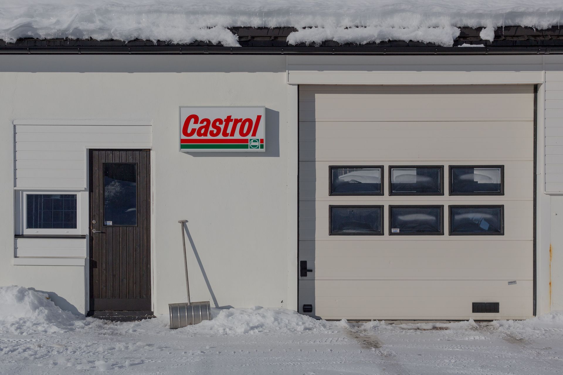 Snowy auto shop exterior with Castrol sign and a garage door