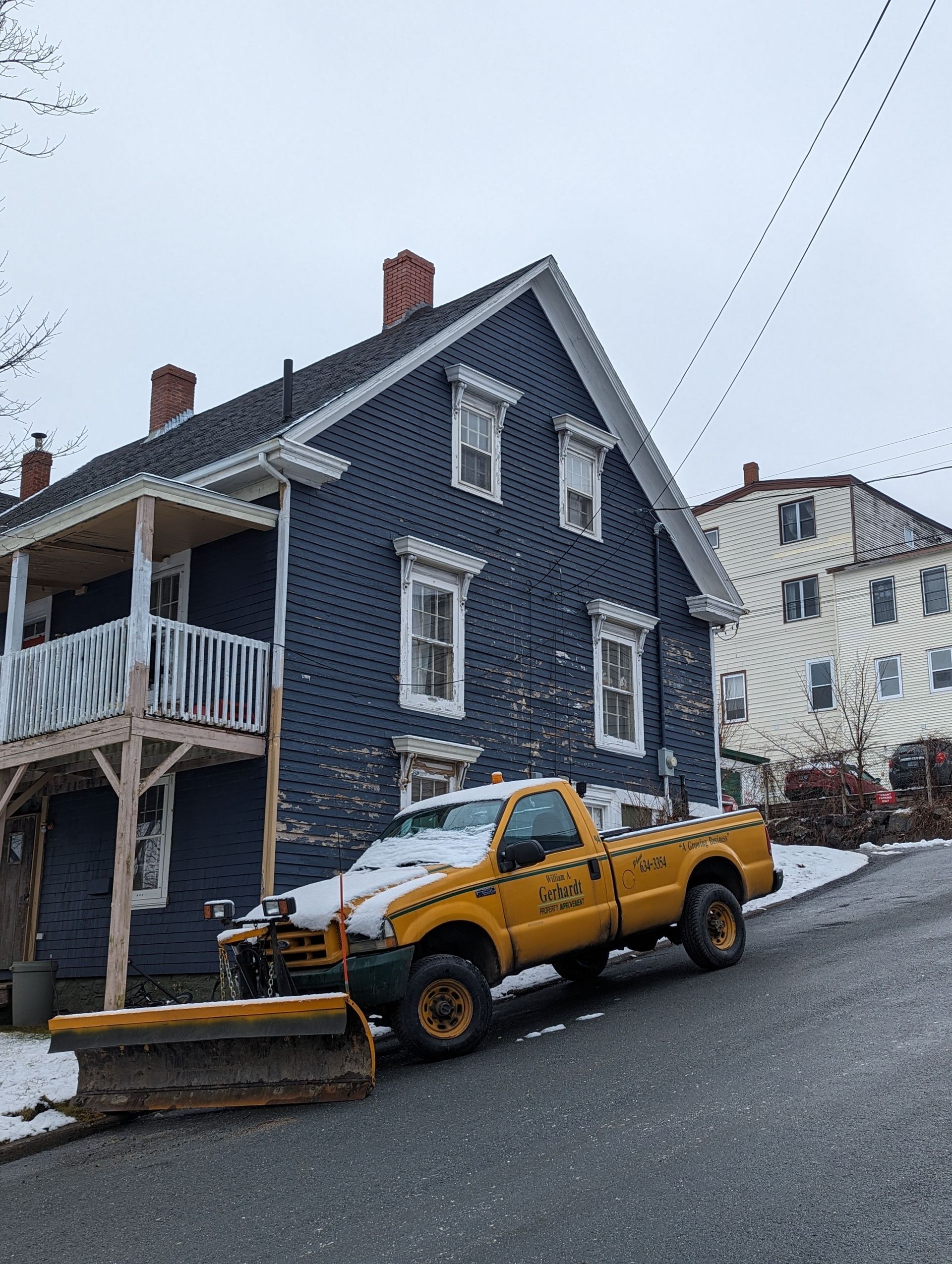 Yellow snowplow on a steep street in light snow.