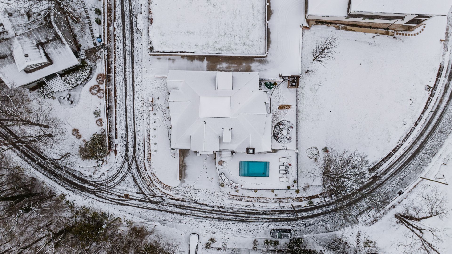 Snow-covered house with a bright blue pool, seen from above