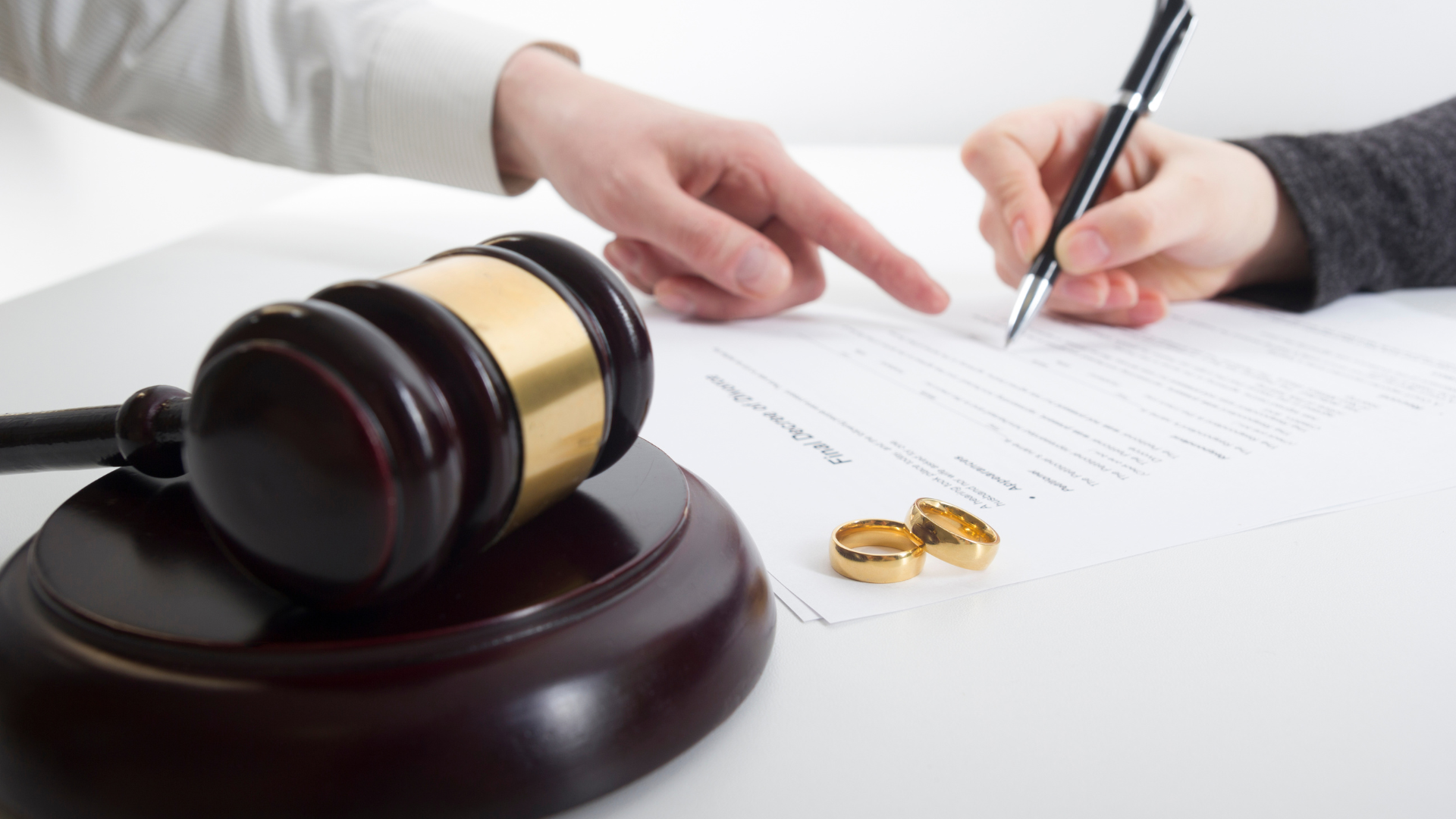 Gavel, wedding rings, and document with hands signing, likely a divorce agreement.