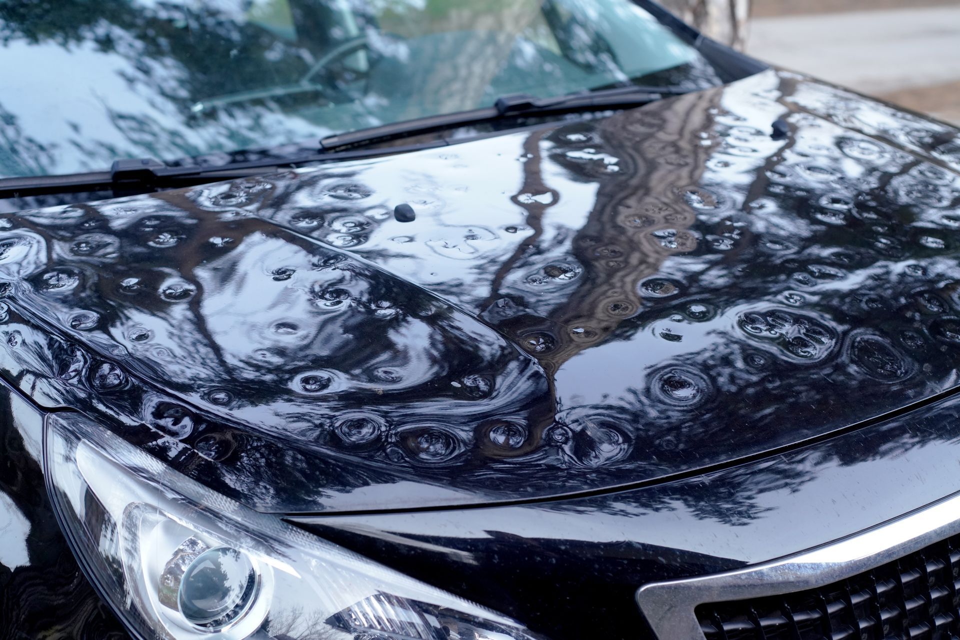 Car hood damaged by hail, showing numerous dents and reflections.