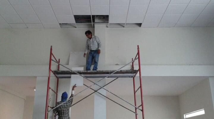 Dos hombres están de pie en un andamio trabajando en un techo.