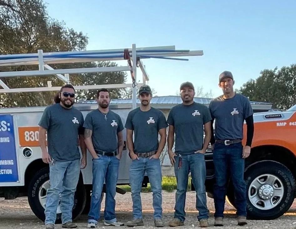 Five plumbers in gray shirts stand in front of an orange service truck outdoors.