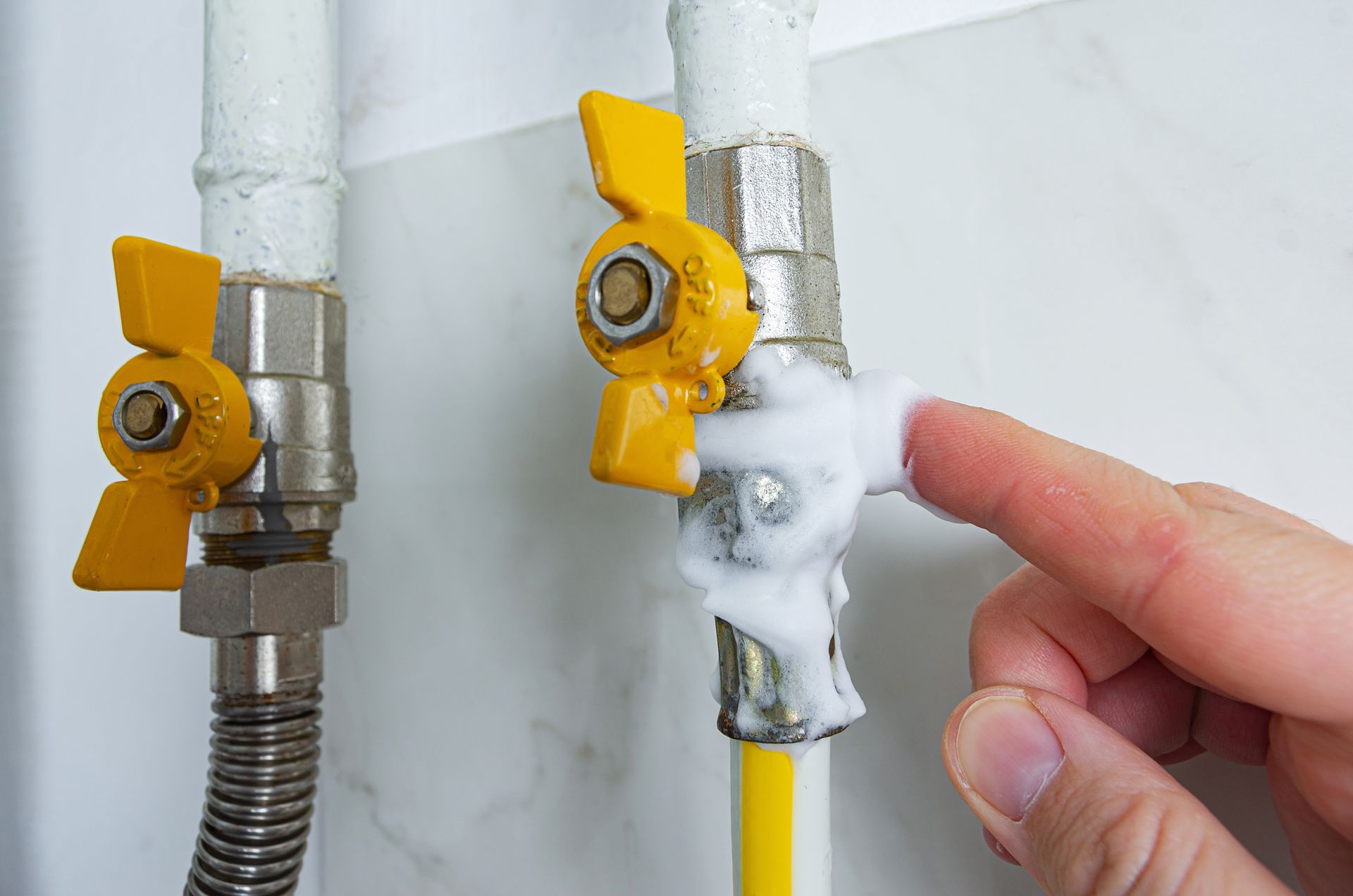 A finger applies soapy foam to a gas valve connection on a pipe to test for a gas leak.