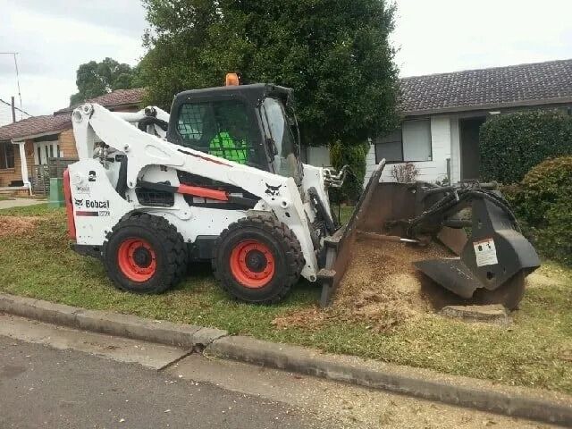 White Bobcat Skid-steer Grinder Grinding Tree Stump on Residential Lawn — D & C Tree Services Pty Ltd in Muswellbrook, NSW
