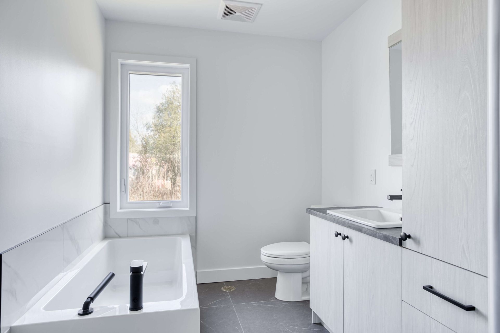 Salle de bain moderne blanche vide avec baignoire, toilettes et meuble-lavabo.