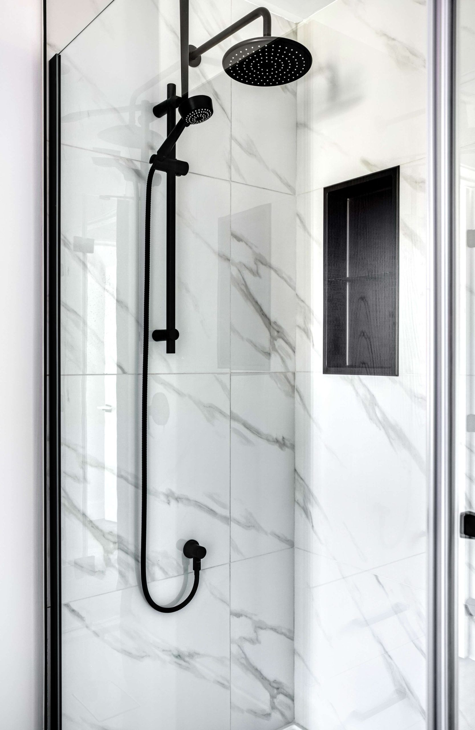 Ensemble de douche noir avec pommeau et douchette contre un mur carrelé en marbre.