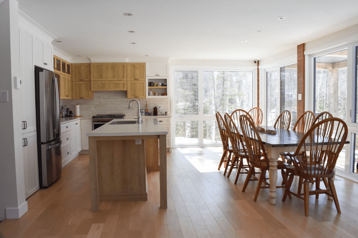 Cuisine et salle à manger à aire ouverte avec plancher et armoires en bois clair, électroménagers en acier inoxydable et grandes fenêtres.