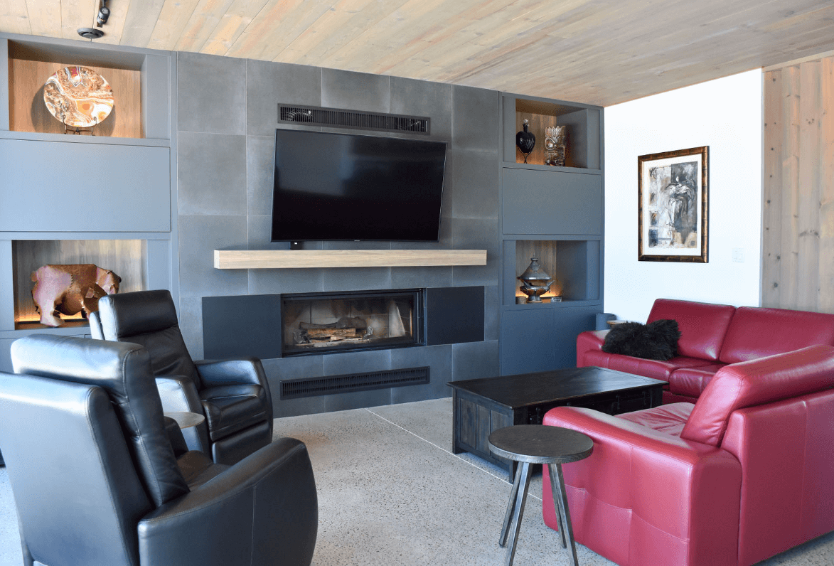 Salon avec cheminée grise, télévision, canapé rouge et fauteuils noirs.