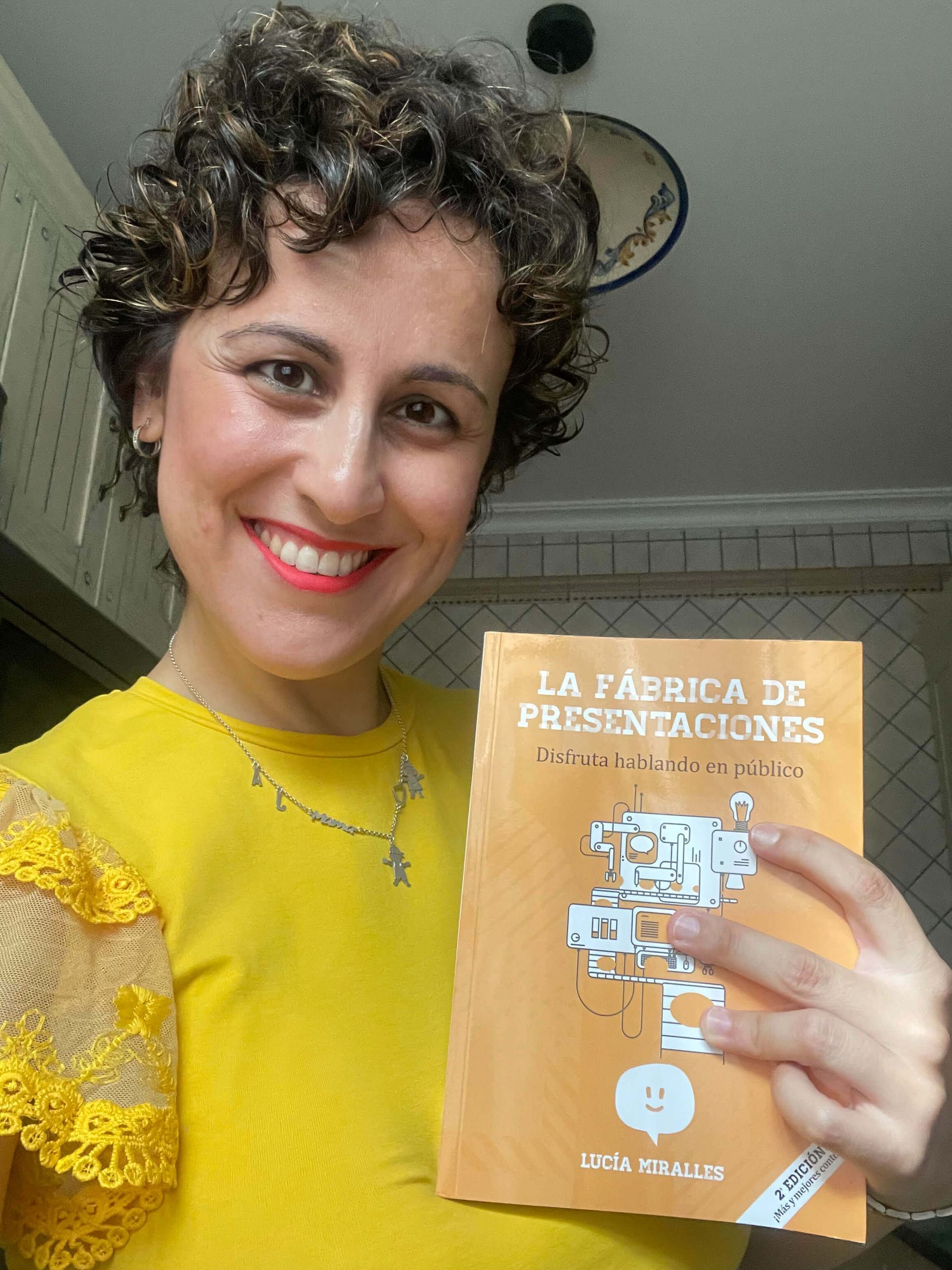 Mujer con cabello rizado sonríe, sosteniendo un libro titulado
