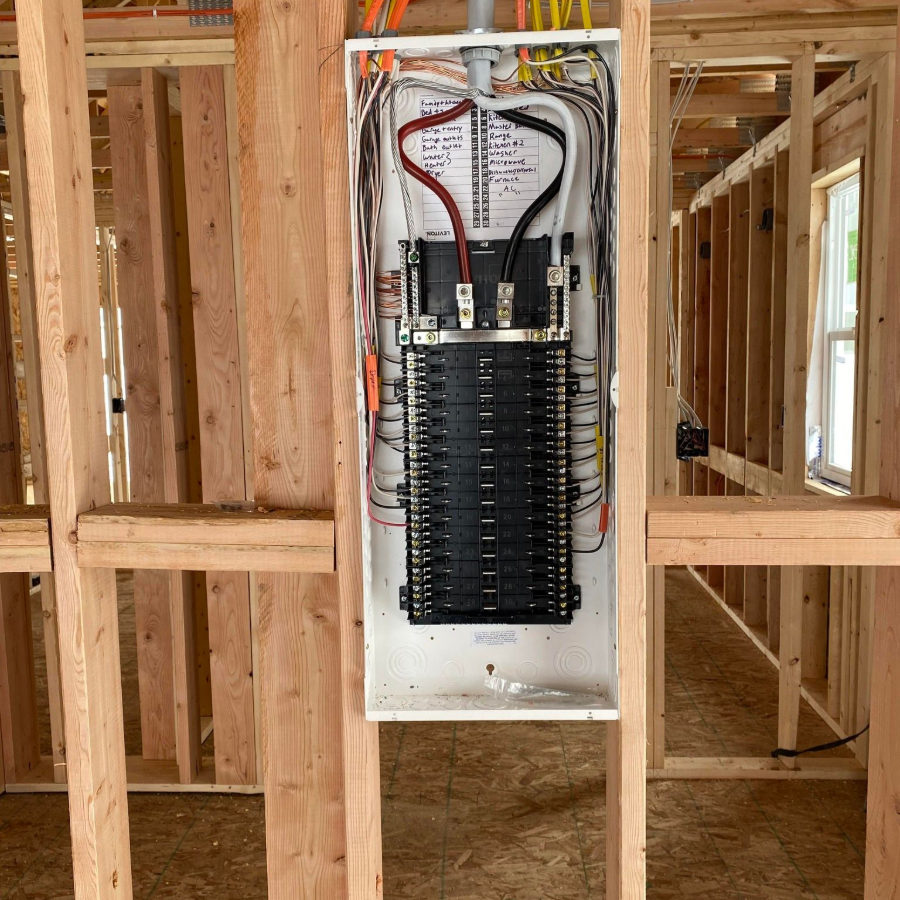 Electrical breaker panel installed in unfinished wall framing with exposed wires and studs