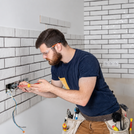 Worker in white hard hat wiring an outlet on a tiled wall during home renovation