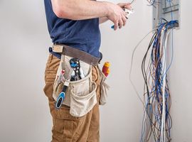 Electrician with tool belt working on exposed wall wiring in a home renovation site