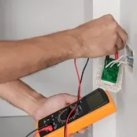 Technician testing wall wiring with a multimeter near an electrical outlet