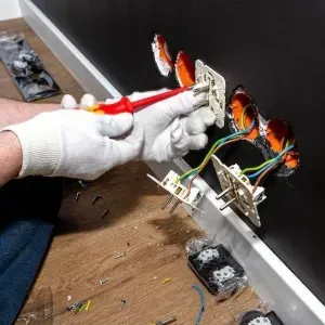 Gloved hands wiring electrical outlets in a wall opening with exposed colorful cables