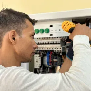 Technician using a drill to work inside an open electrical control panel.