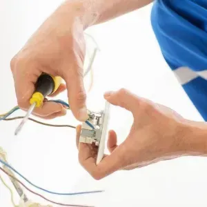 Hands wiring an electrical outlet with a screwdriver and exposed cables