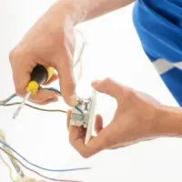 Hands wiring an electrical outlet with a screwdriver and exposed cables