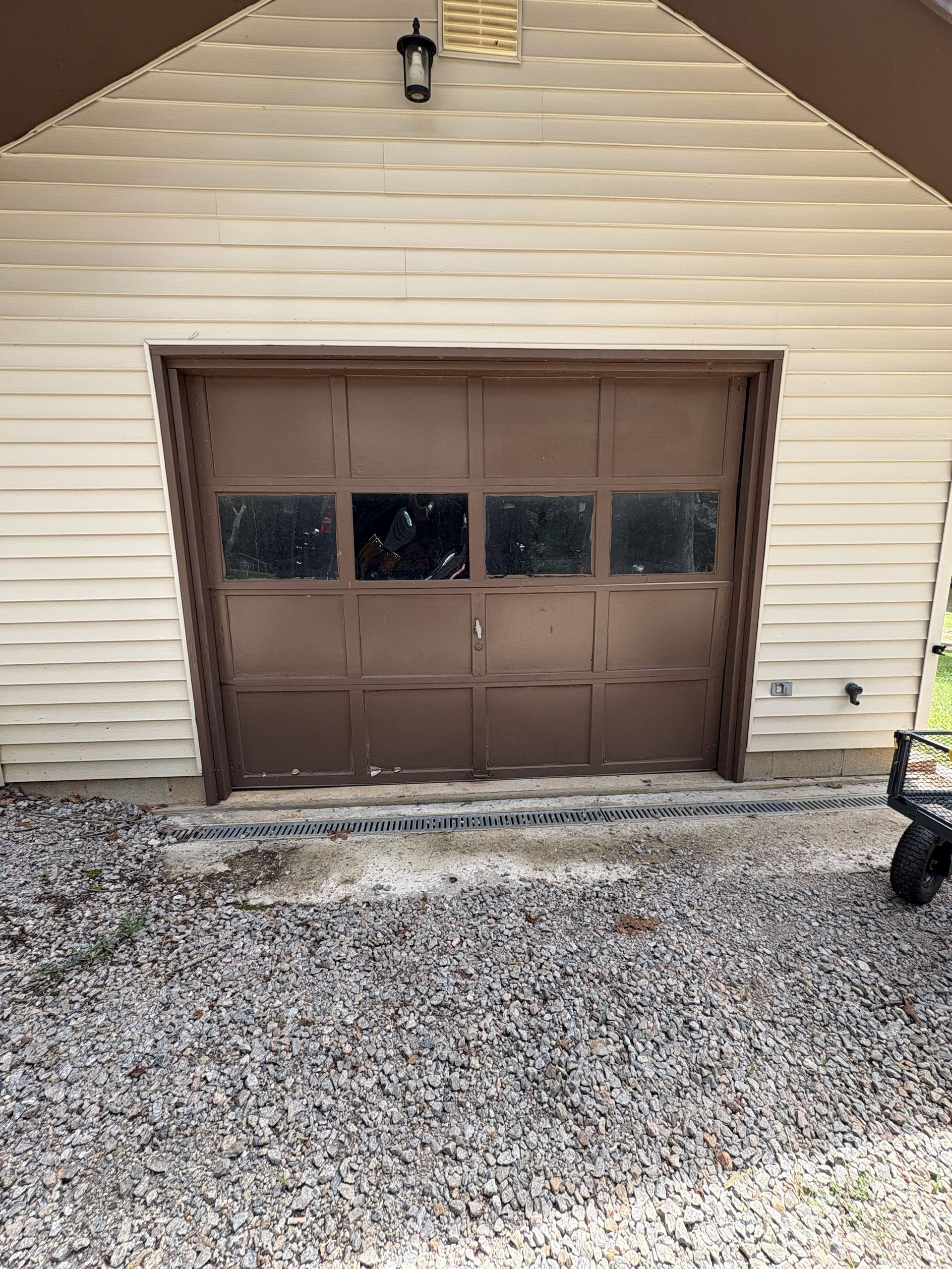 A person in blue gloves uses tools on a broken car spring in a garage.