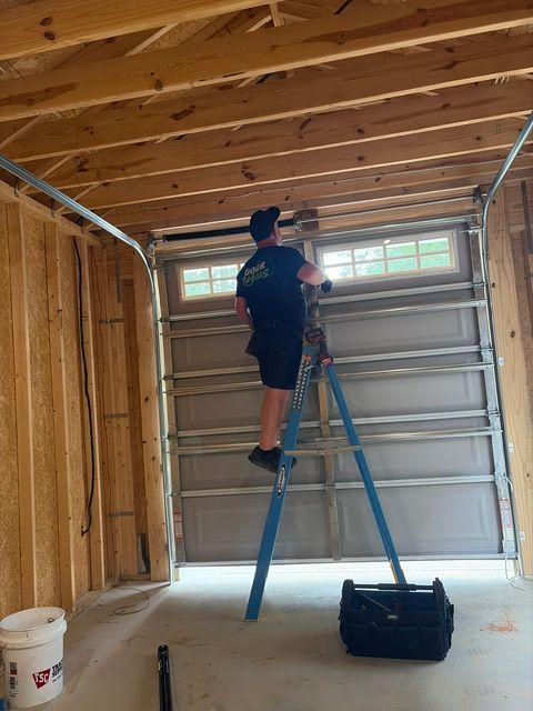 Garage door technician in blue overalls testing a white garage door with a laser, holding a clipboard.