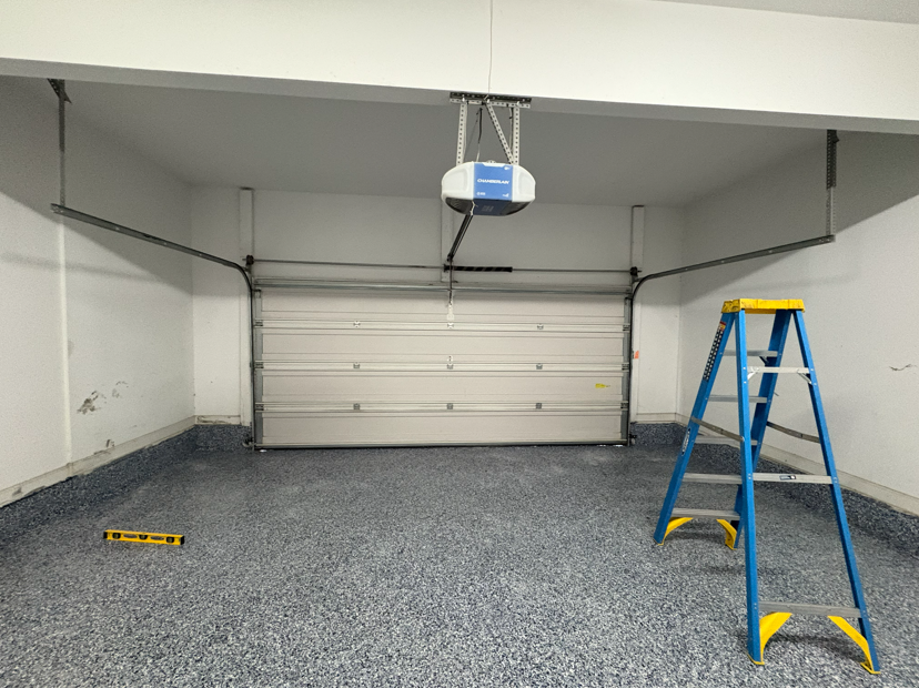 Two men in blue shirts in a garage looking at a phone, pointing at the screen, with a garage door opener above.