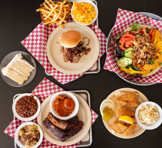 Assorted fast food dishes on checkered trays, including burgers, fries, pasta, and desserts.