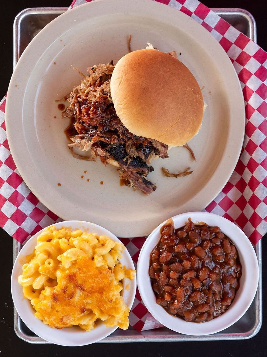Plate with a sandwich, macaroni and cheese, and baked beans on a checkered tray mat.