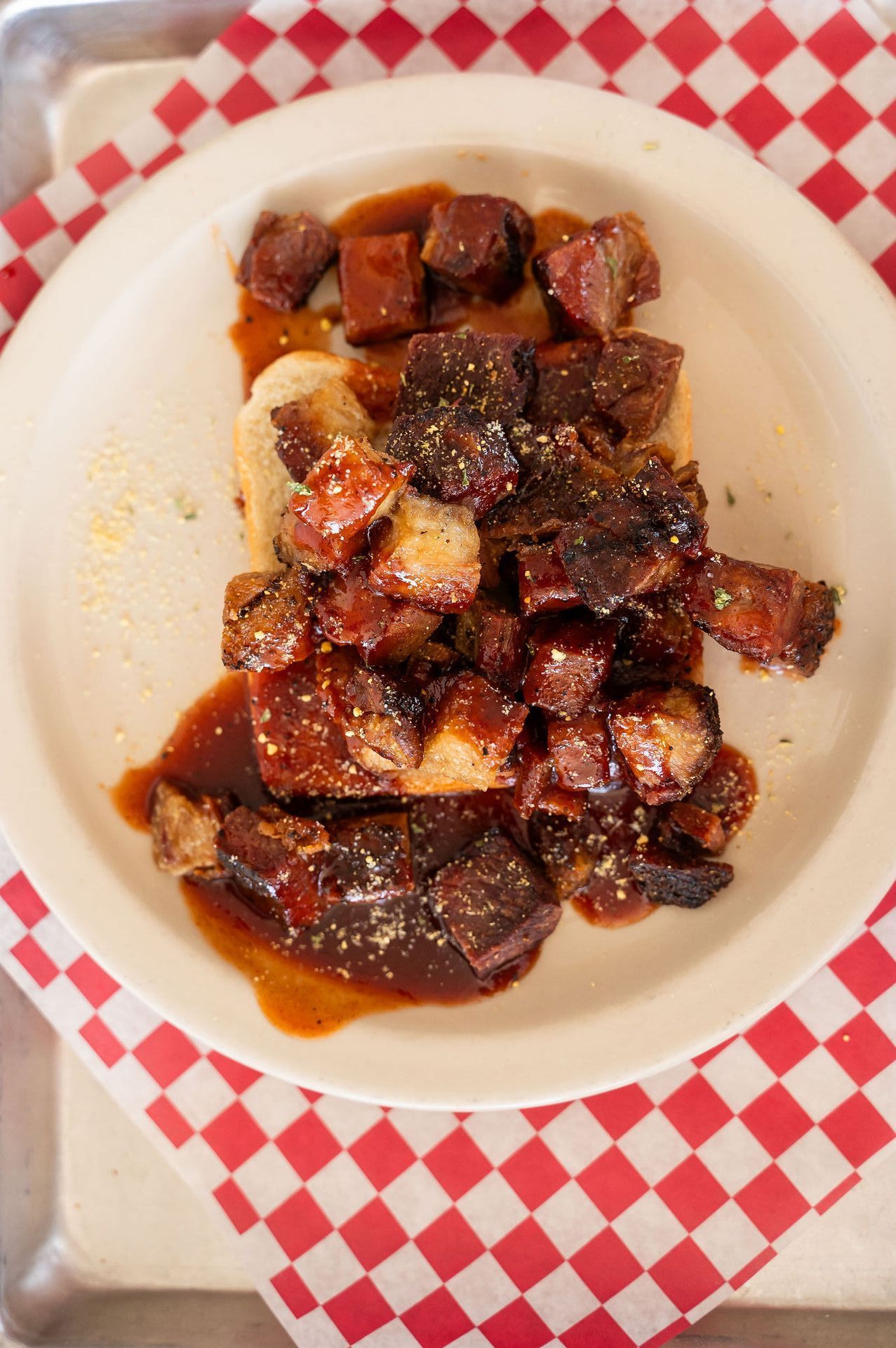 A bowl of dark saucy meat chunks on a red-and-white checkered cloth.