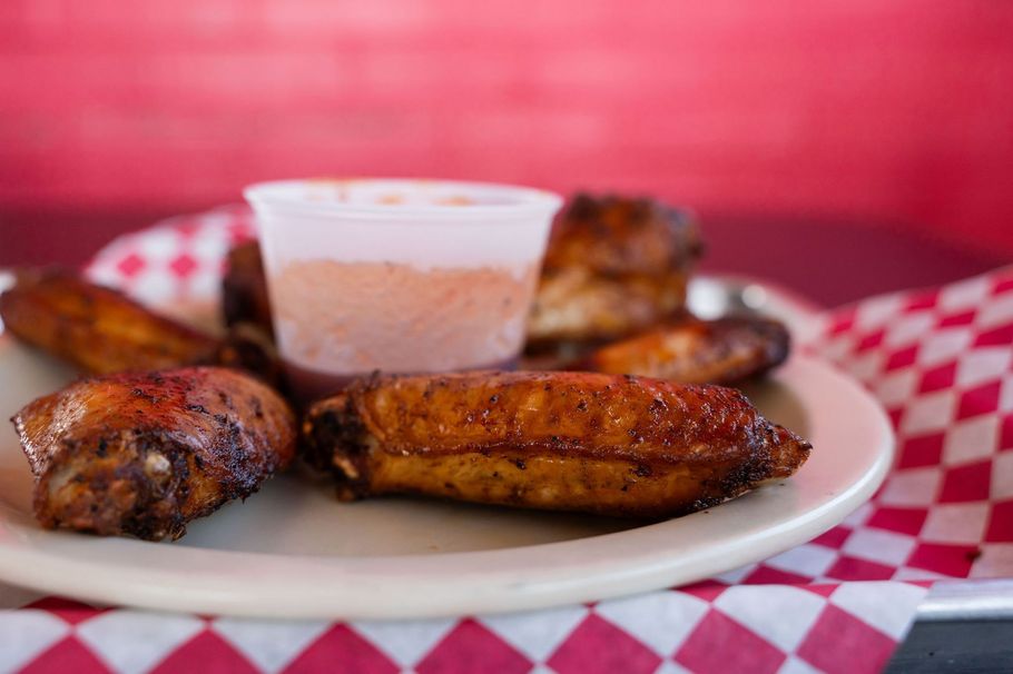 Plate of grilled chicken wings with dipping sauce on a red-and-white checkered tablecloth