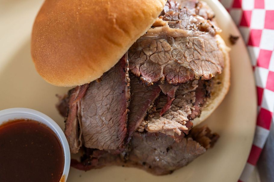 Sliced roast beef sandwich on a bun with barbecue sauce in a paper-lined basket