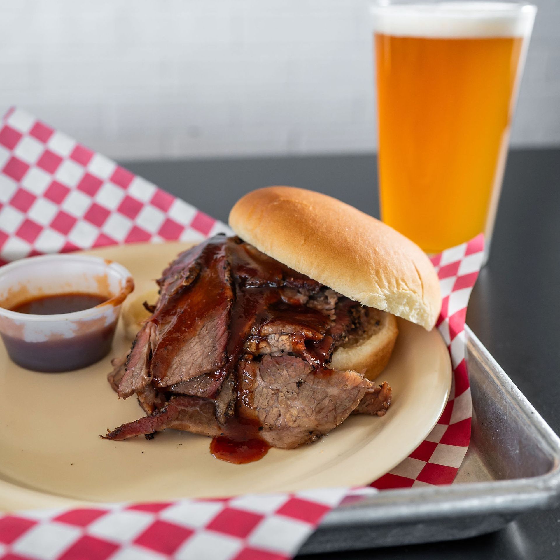 Barbecue sandwich with sauce and a beer on a tray with red-checkered paper