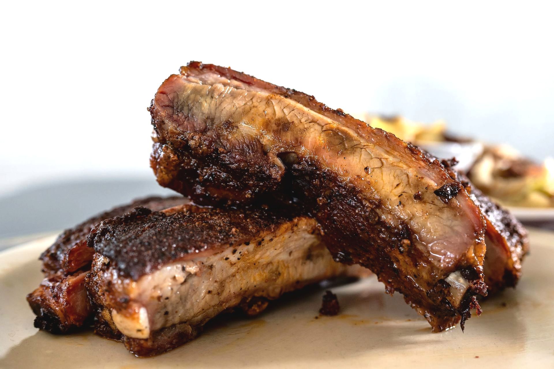 Two grilled barbecue ribs stacked on a plate, glazed and charred