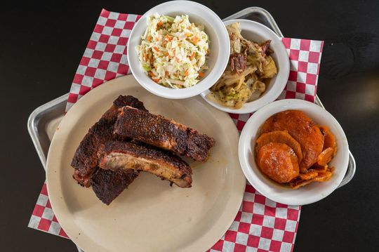 Barbecue meal with ribs, coleslaw, sides, and beans on a red checkered placemat