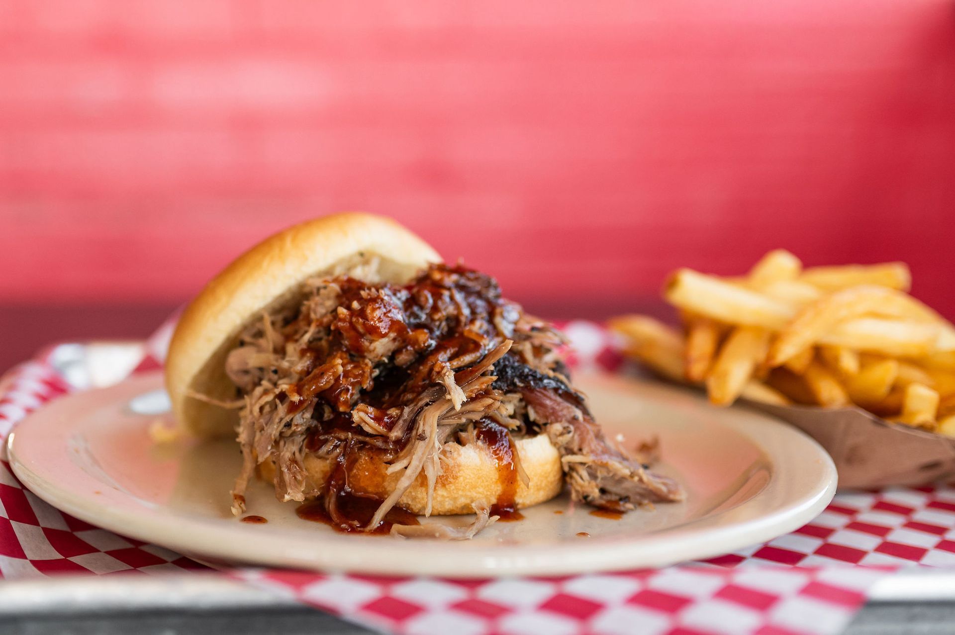 Barbecue pulled pork sandwich on a plate with fries on a red checkered tablecloth