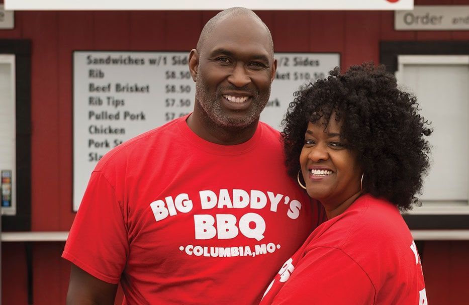 Smiling couple in red Big Daddy’s BBQ shirts standing in a restaurant.