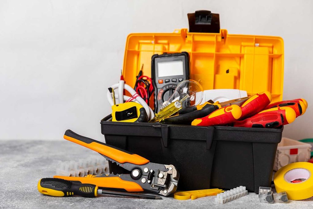 An open yellow and black toolbox filled with electrical tools, including a multimeter, pliers, and yellow electrical tape.