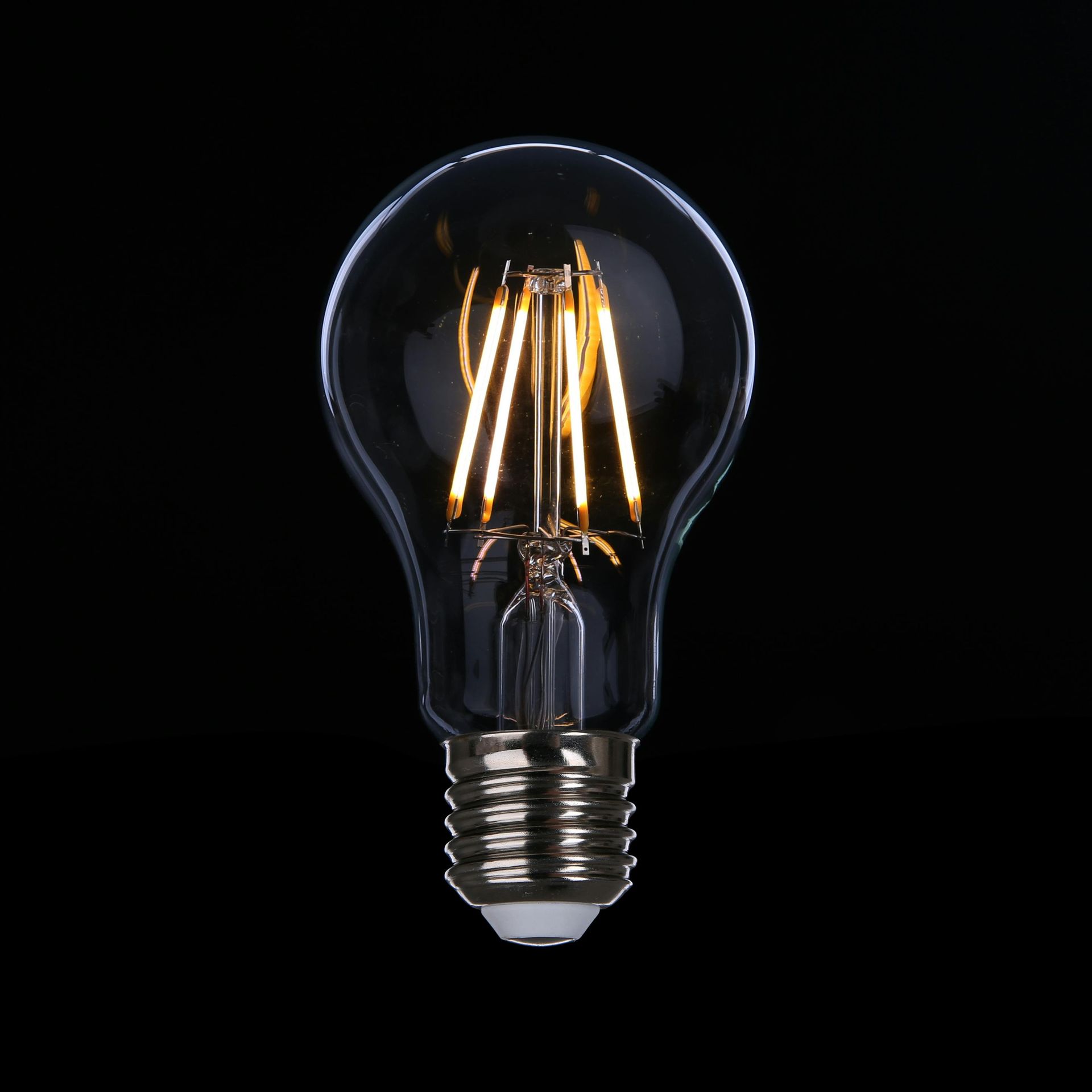 A clear LED filament light bulb glows warmly against a black background.
