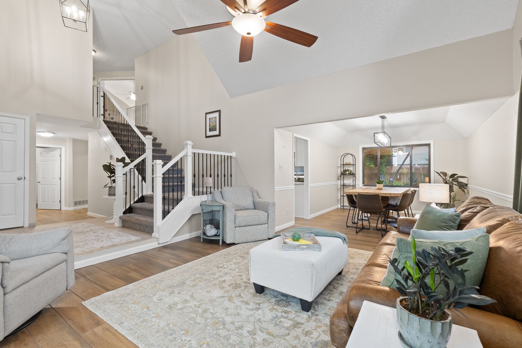 A living room with a staircase, seating, dining table, and hardwood floors.