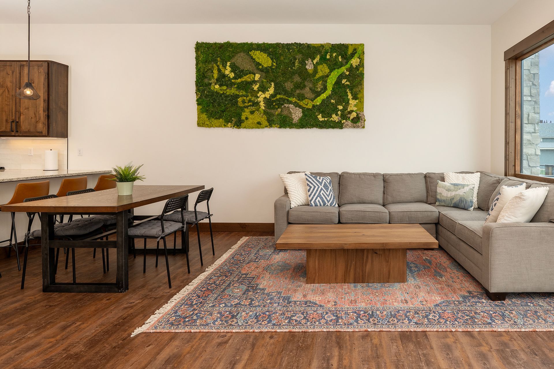 Modern living room with a sectional sofa, dining table, and a moss wall art piece.