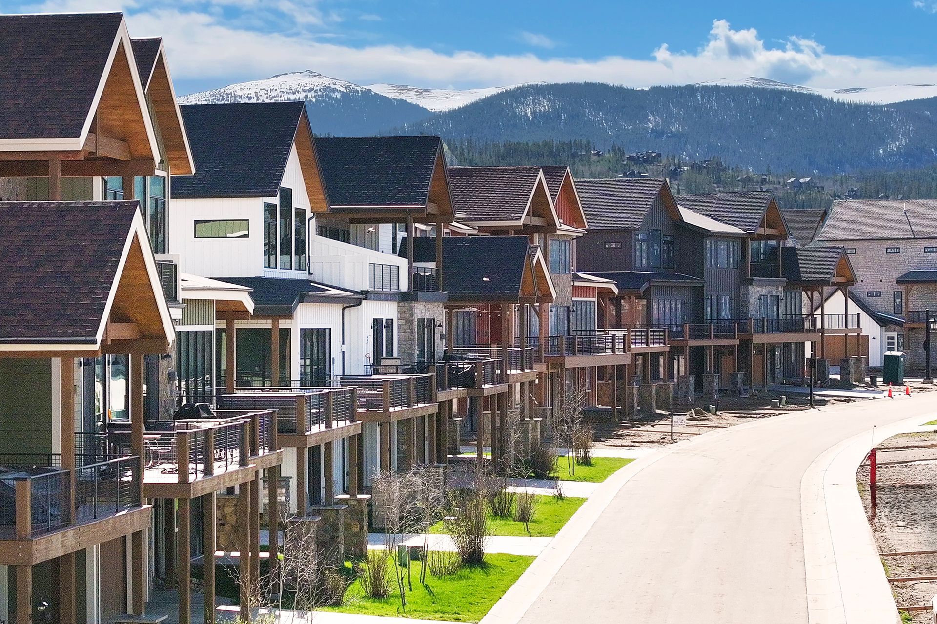 Row of multi-story homes with balconies, brown roofs, and mountain backdrop.