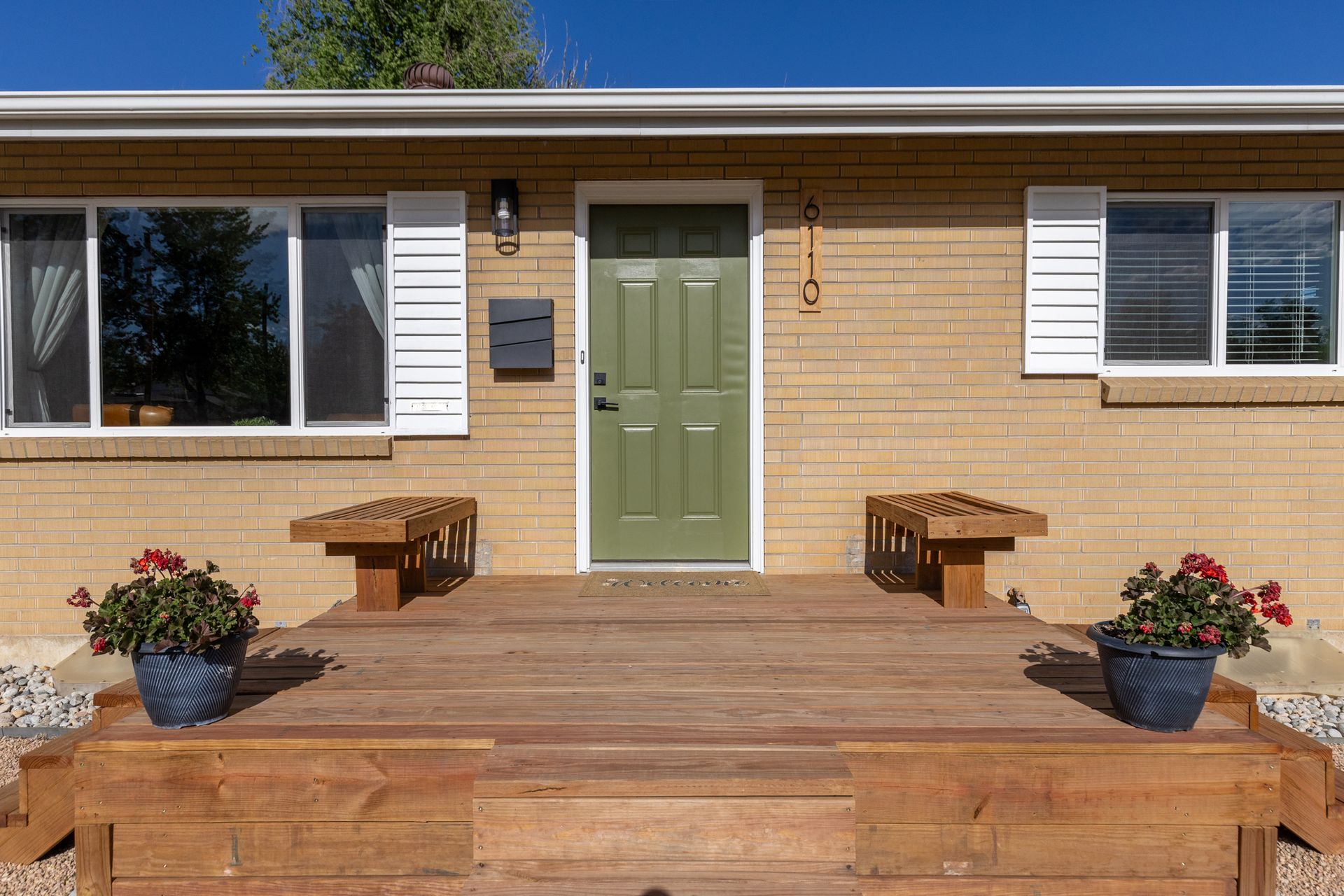 Front porch with green door, wooden steps, benches, and potted flowers on a brick house