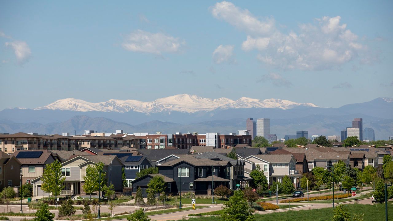 Houses with mountain range and city skyline under a blue sky with clouds.