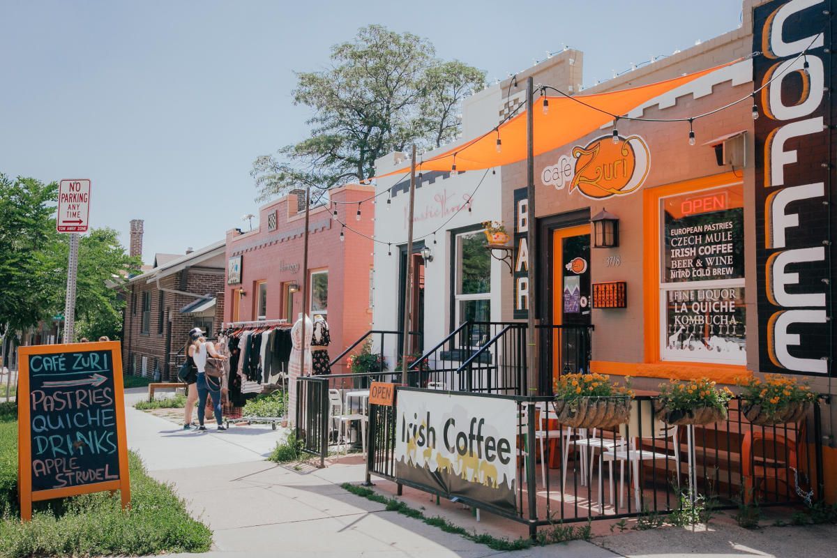 Colorful storefronts of Lush Coffee and other businesses on a sunny street with pedestrians.