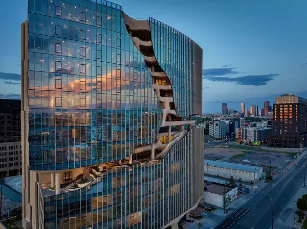 Modern glass skyscraper with a curved cutout, reflecting a sunset over a city.